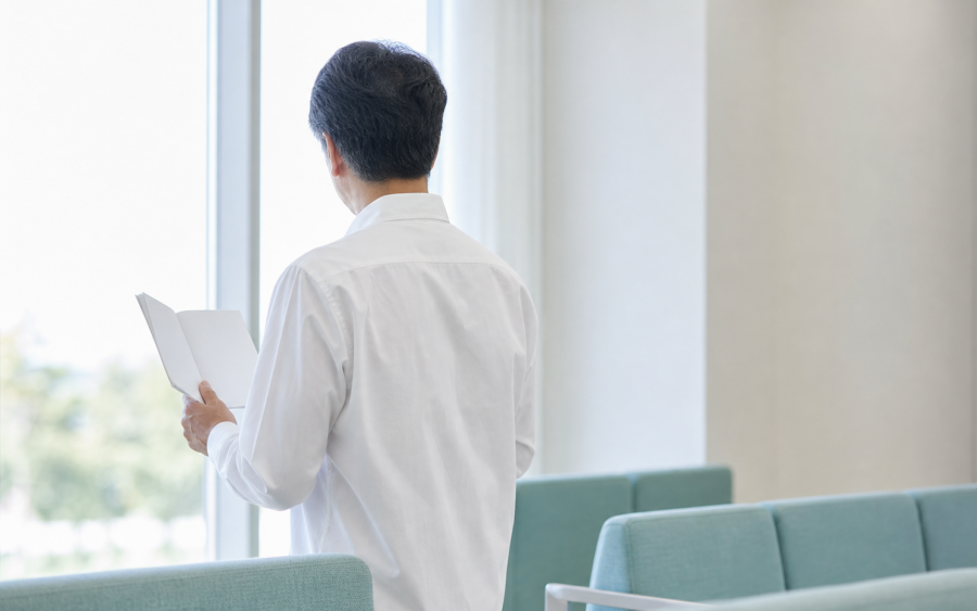 밝은 대기 공간에서 안내 책자를 들고 서 있는 중년 남성의 뒷모습